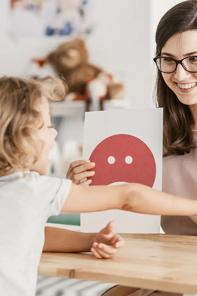 As part of her social emotional regulation occupational therapy session, a young girl points to an emotion printed on a sheet of paper to indicate how she is feeling.